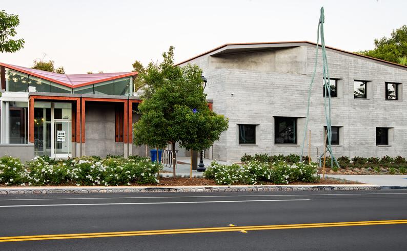 street view of a building with a tall sculpture in front adjacent to palm trees